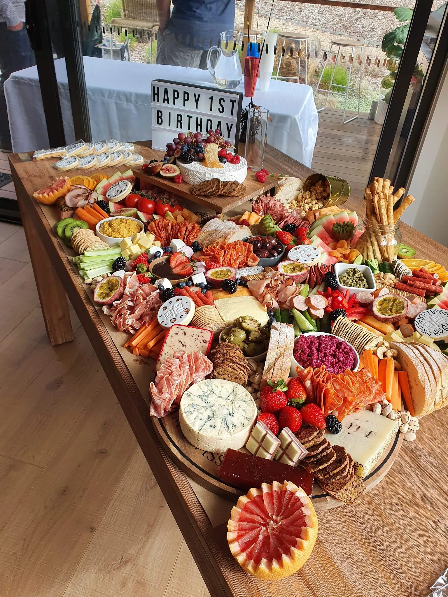 Full-length grazing table at a birthday event, loaded with charcuterie, cheese, fruit, and dips