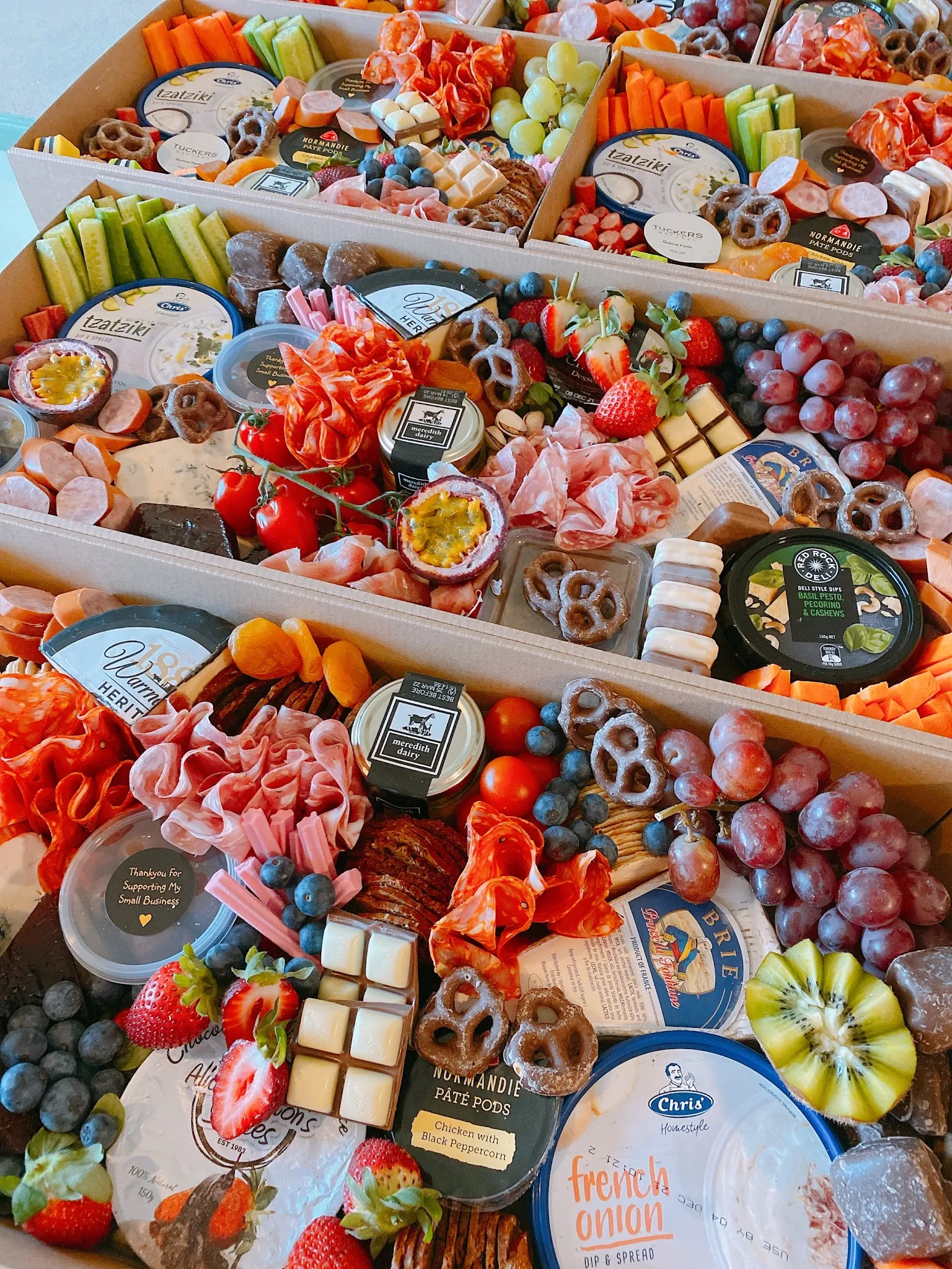 Three open Coastal Grazing boxes packed with colourful charcuterie, fruit, dips, and crackers